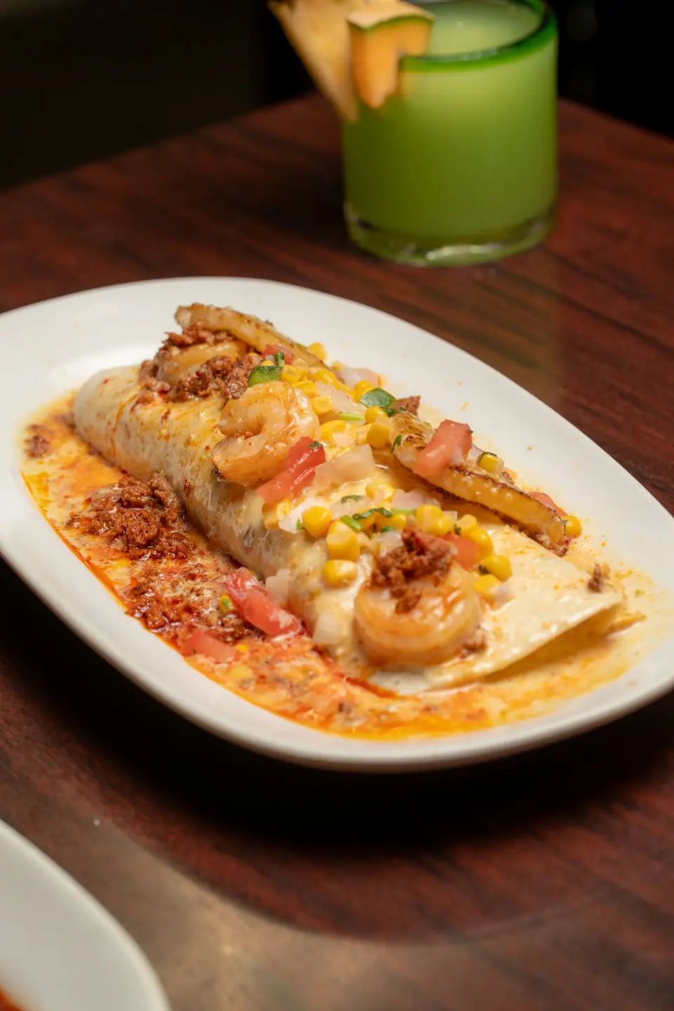 Burrito topped with shrimp, corn and chorizo, with a green drink